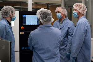 Photo of masked researchers standing in front of a 3D printer